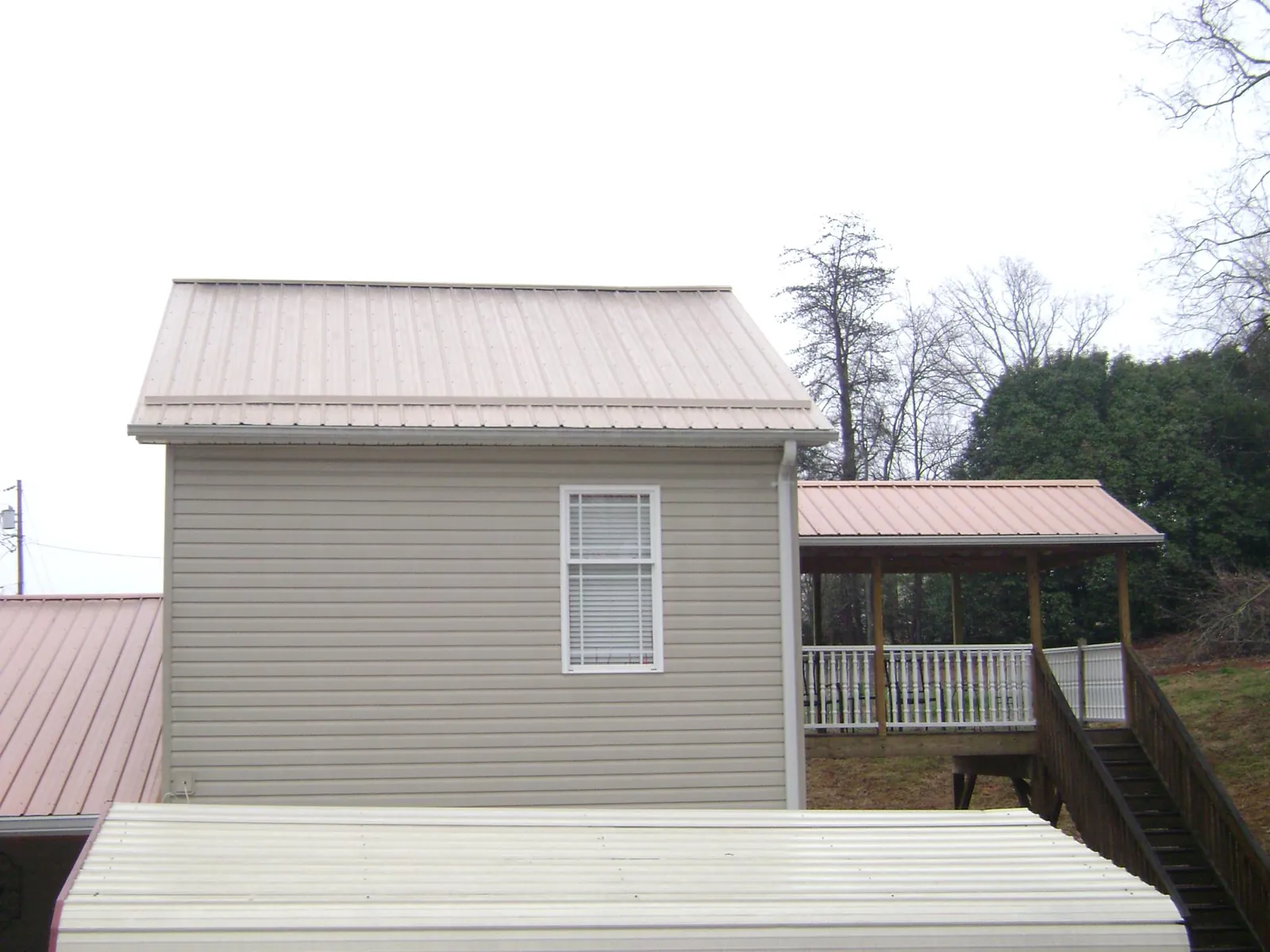 Tan metal roofs on a two story addition and attached porch, from a Roof Replacement job in Cumberland